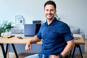 Confident smiling man in blue shirt resting arm on desk, limited company concept