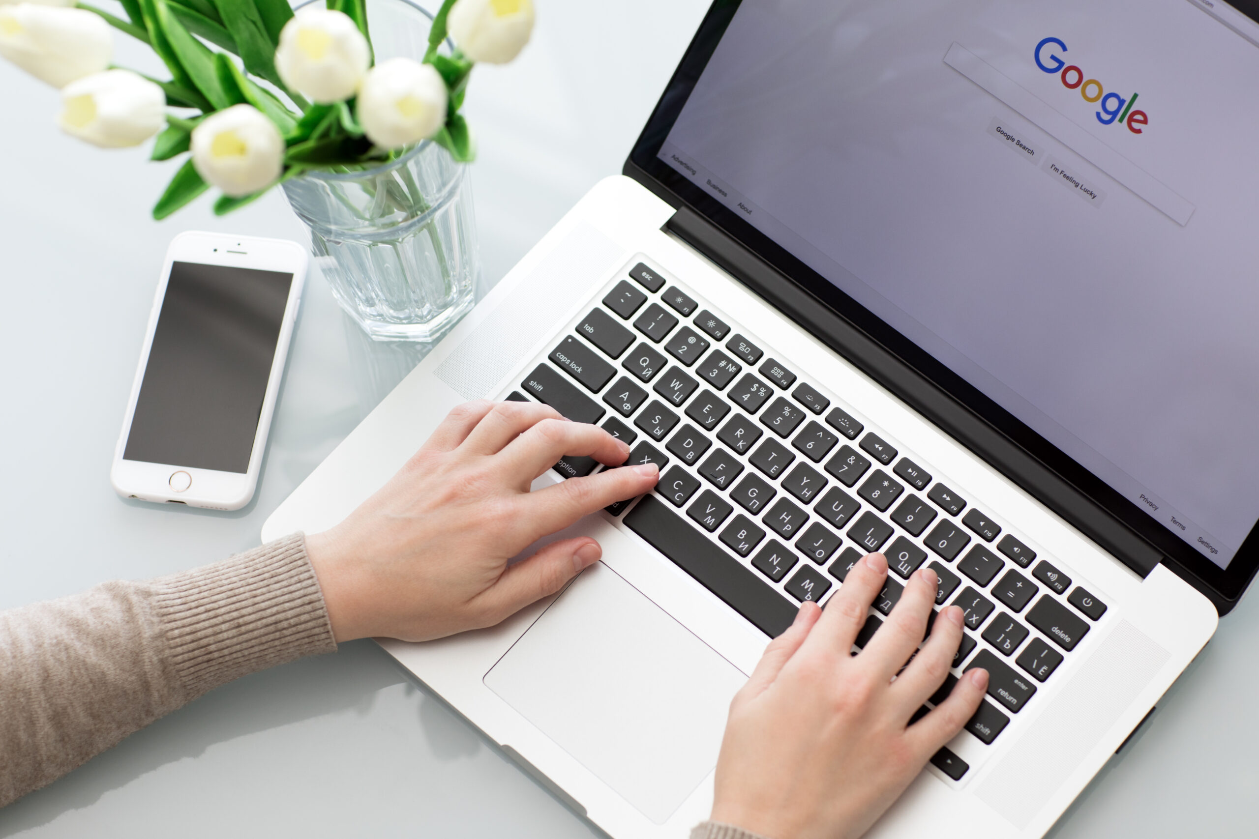 Woman searching Google on laptop beside vase of flowers