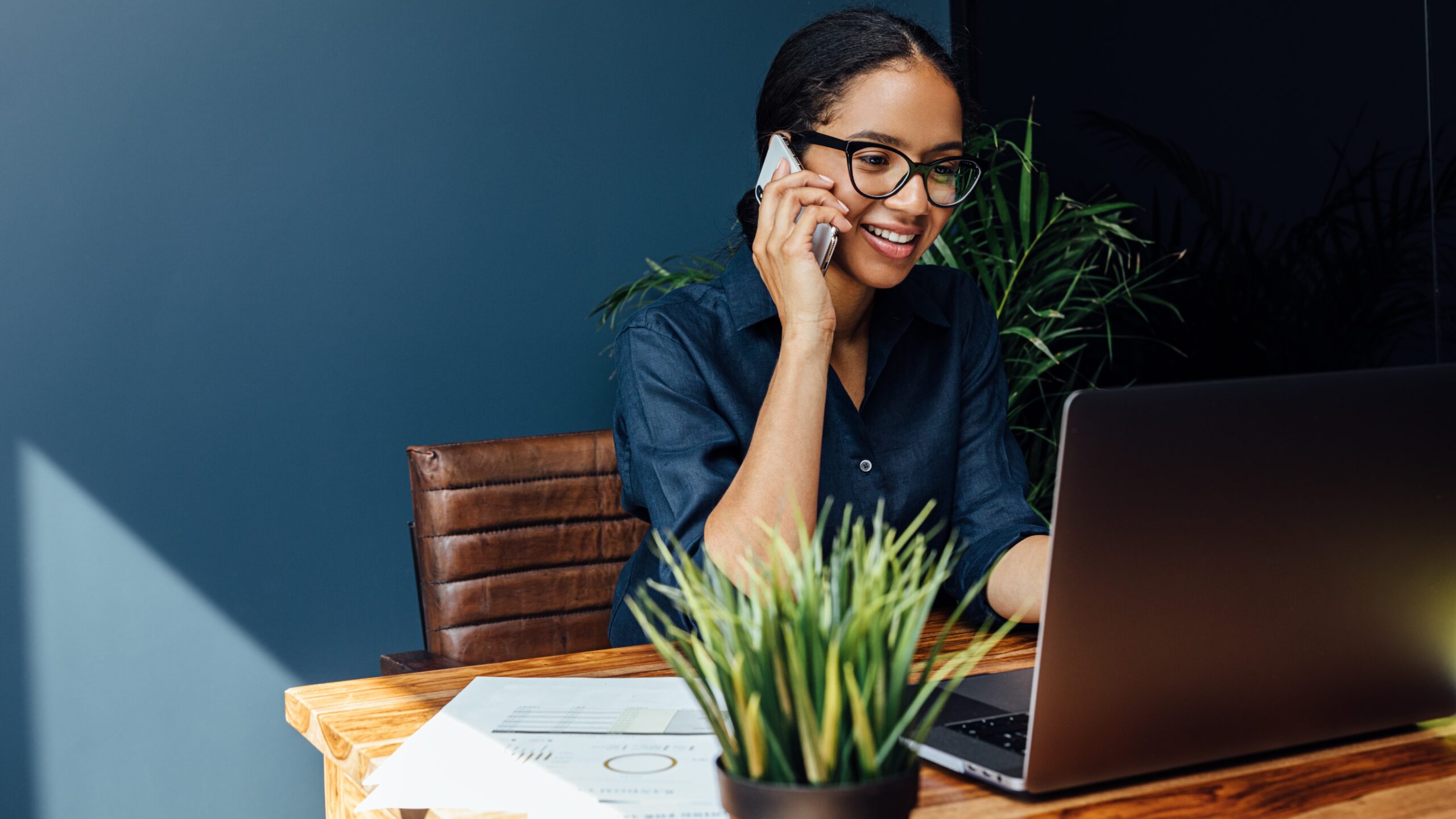 Young woman sitting behind laptop while on mobile phone, freelancer concept