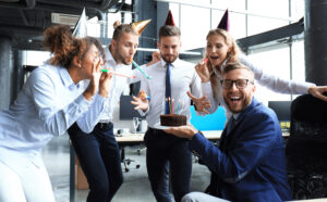 office worker celebrating birthday in office being given cake, your first year in business concept