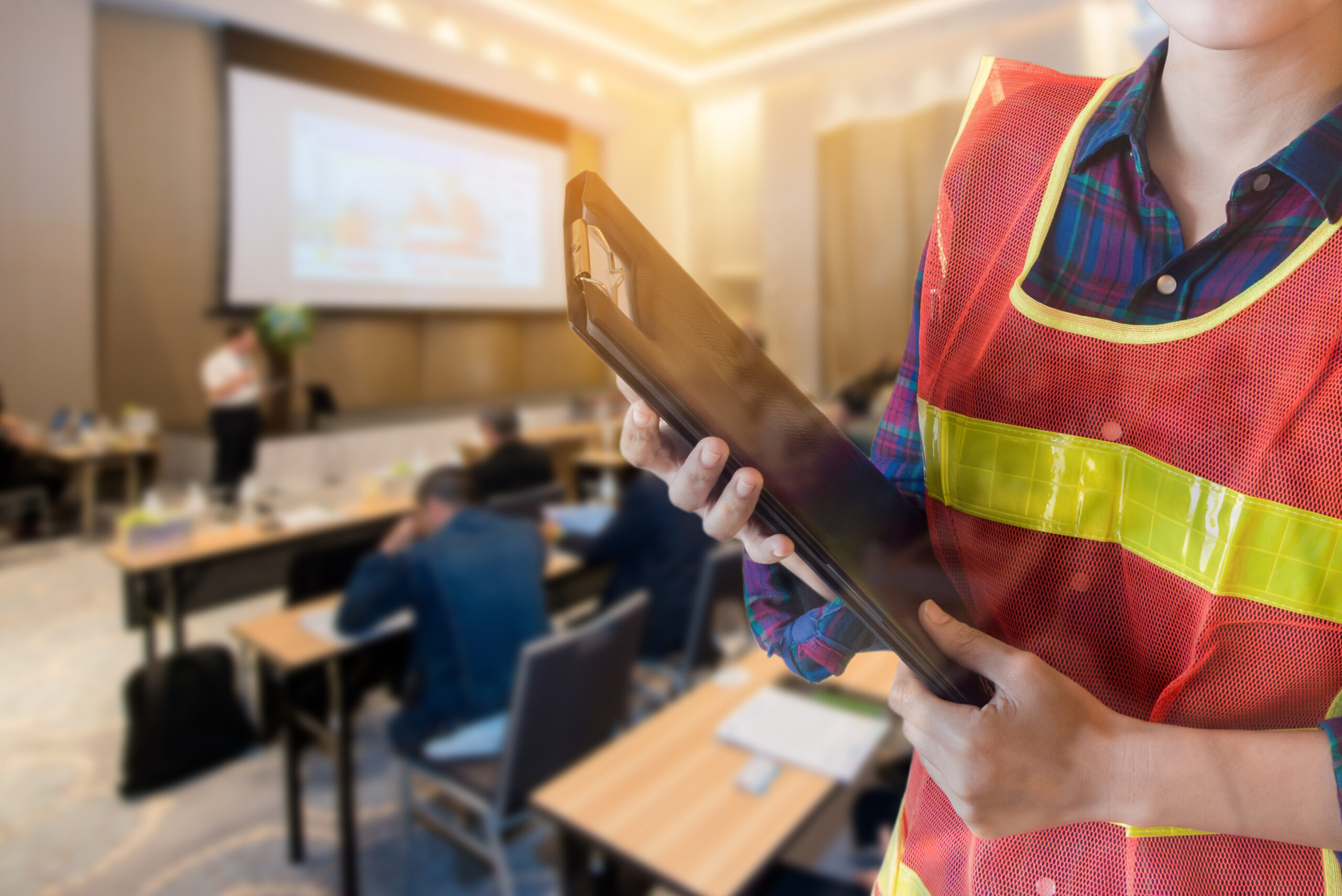 Woman in hi-vis holding clipboard, health and safety seminar