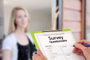 Person standing at door holding market research questionnaire on clipboard, door answered by blonde woman