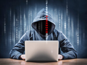 Hooded hacker poised over laptop