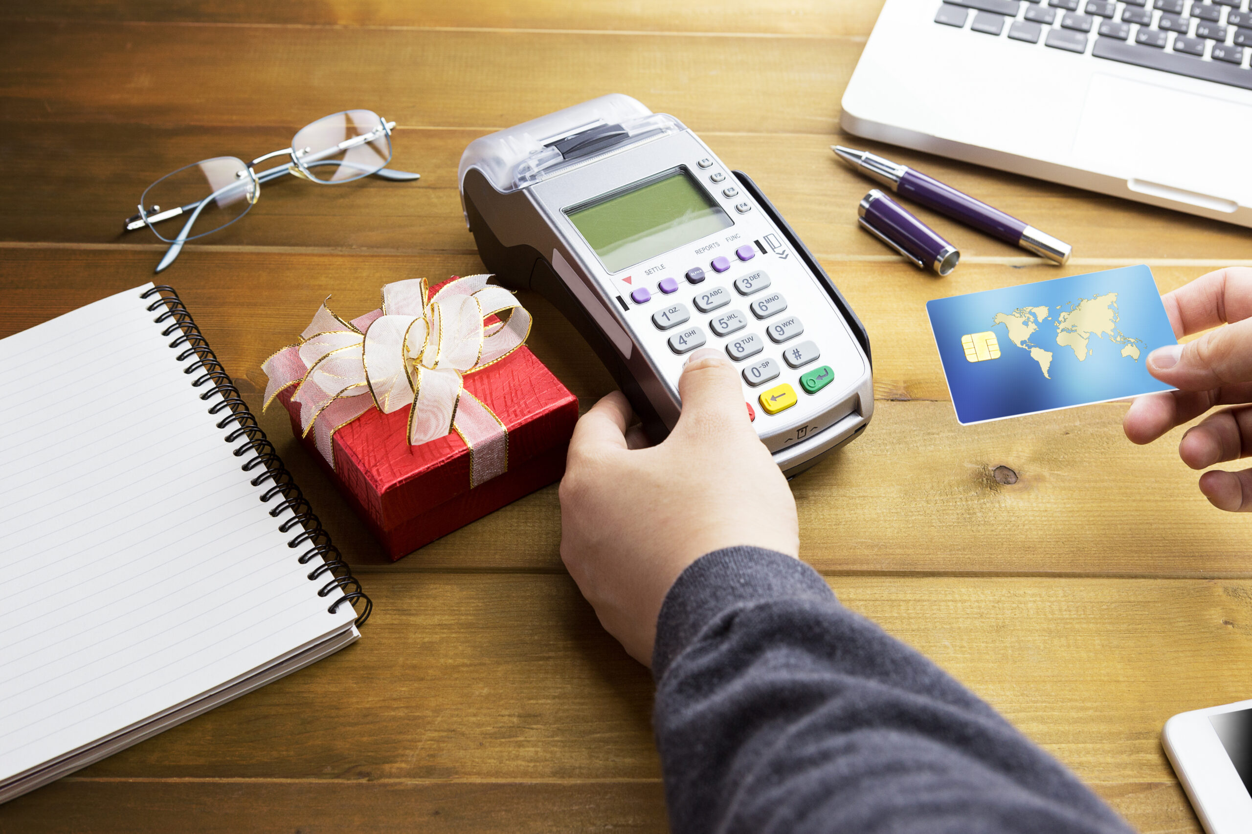 POS system concept. Cashier hand holding a credit card over EDC machine or credit card terminal with calculator and glasses