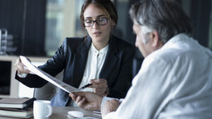 Young female bespectacled woman showing document to older man, hiring accountant concept