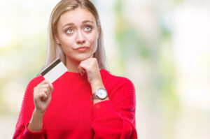Young blonde woman holding credit card over isolated background serious face thinking about question, best payment processors concept