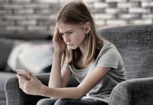 Sad teenage girl with smartphone at home, The UK Domain Samaritans concept