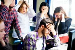 Young people clutch their heads standing over bearded colleague who's made a mistake, start-up mistakes concept