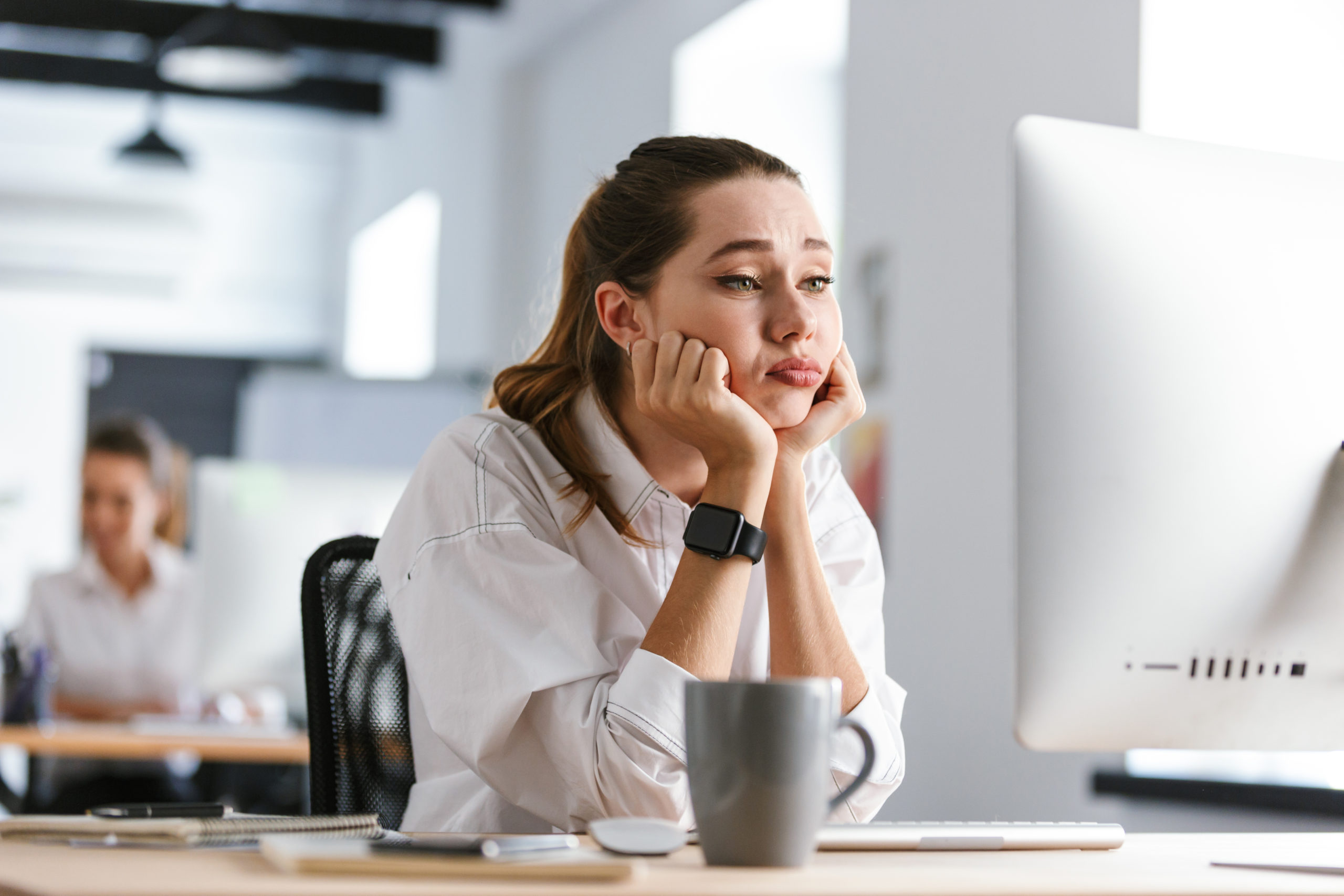 Bored young woman dressed in shirt sitting at her workplace, escaping the nine to five concept