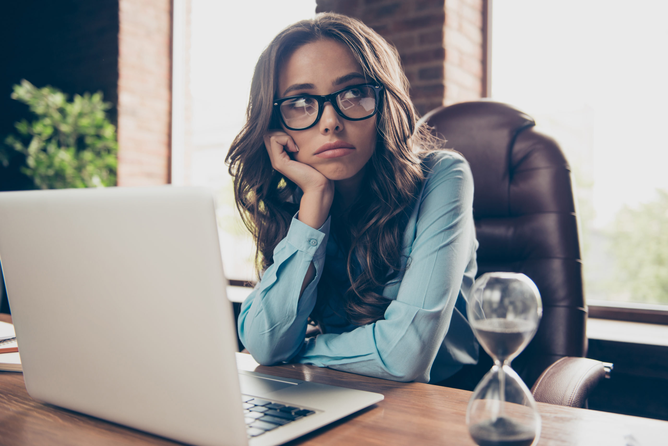 Businesswoman cupping head waiting, hourglass timer on desk, small business grants concept
