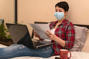 young woman sitting on bed wearing face mask self-isolating, business self-isolating concept