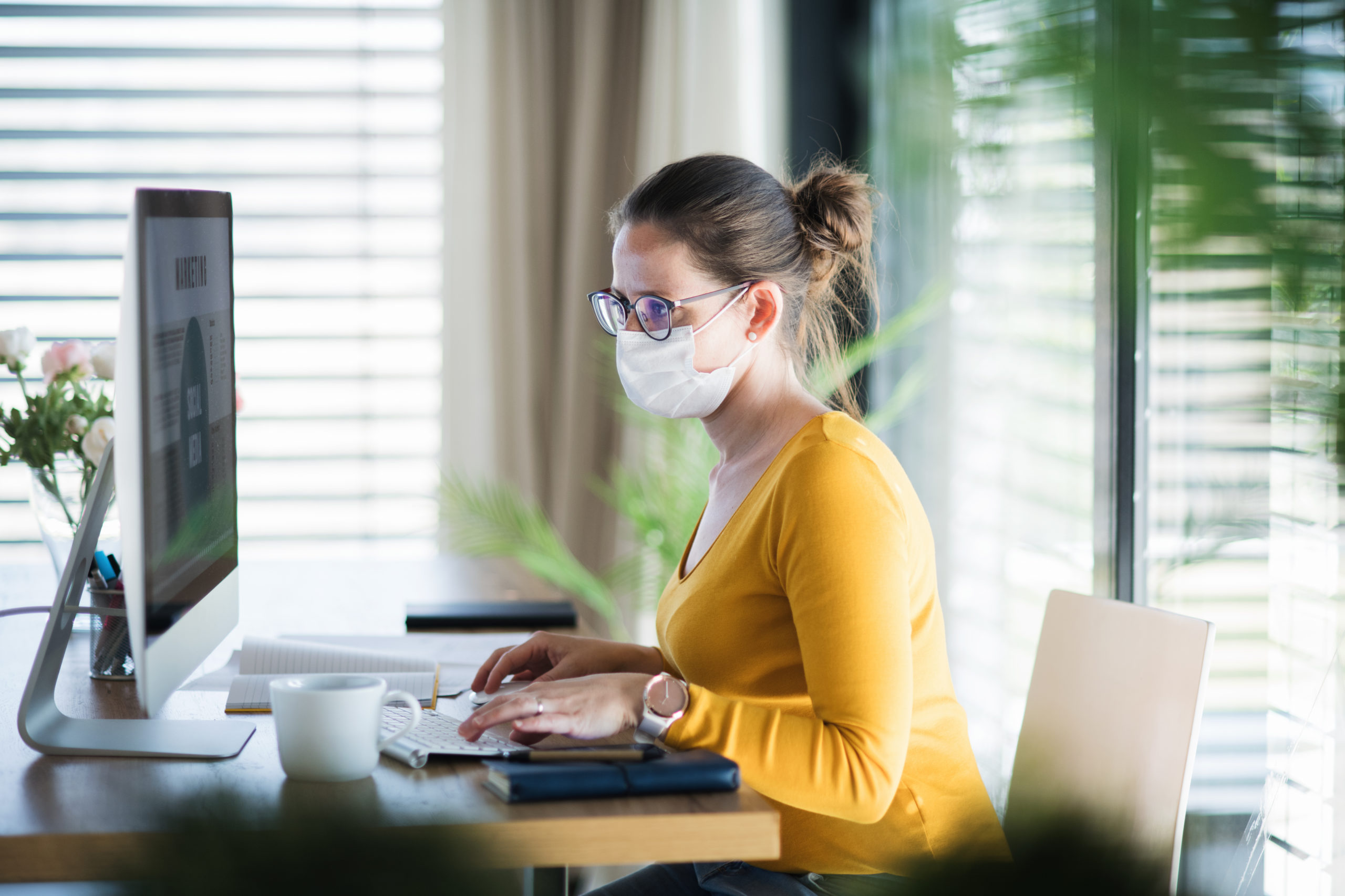 woman in face mask sitting at computer, self-employed income support concept