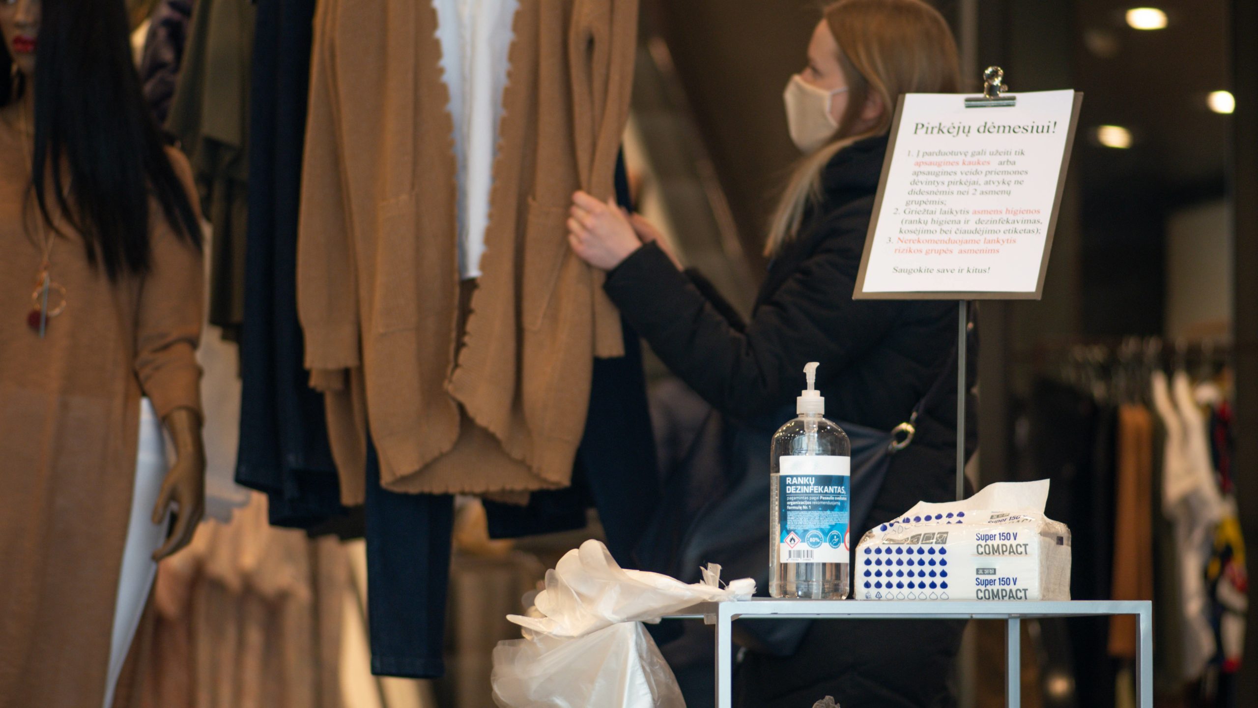 young woman wearing facemask adjusting mannequin in shop window, shop PPE concept