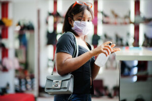 Young black woman in shoe shop wearing facemask and using hand sanitiser, shops reopen concept