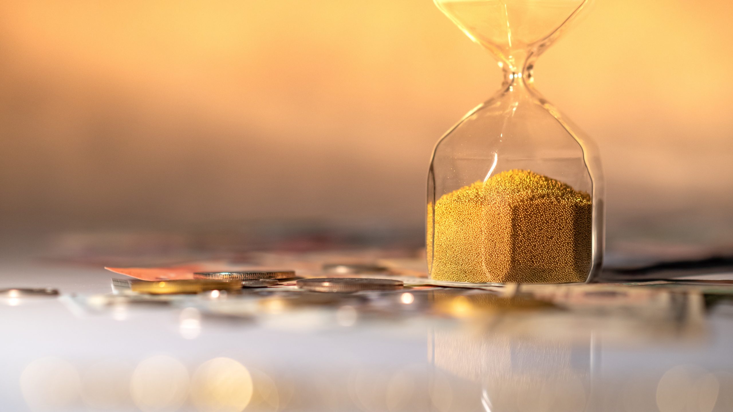 Reflection of hourglass running out of time on glowing table with currency. Bounce Back Loan concept
