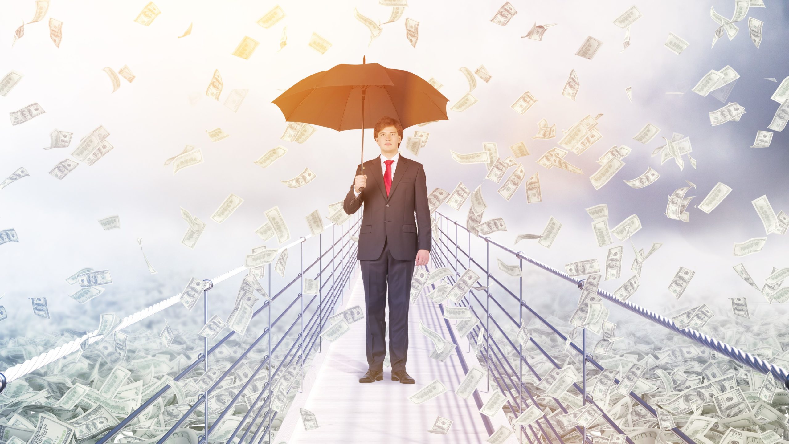 Businessman standing on bridge being rained on by money holdiing umbrella, bridging finance concept
