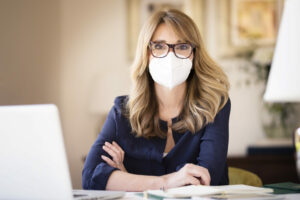 Middle aged woman wearing face mask while working at home, self-employed grant concept
