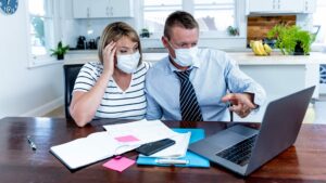 Stressed couple in kitchen wearing facemasks studying laptop, Covid-19 business loan concept