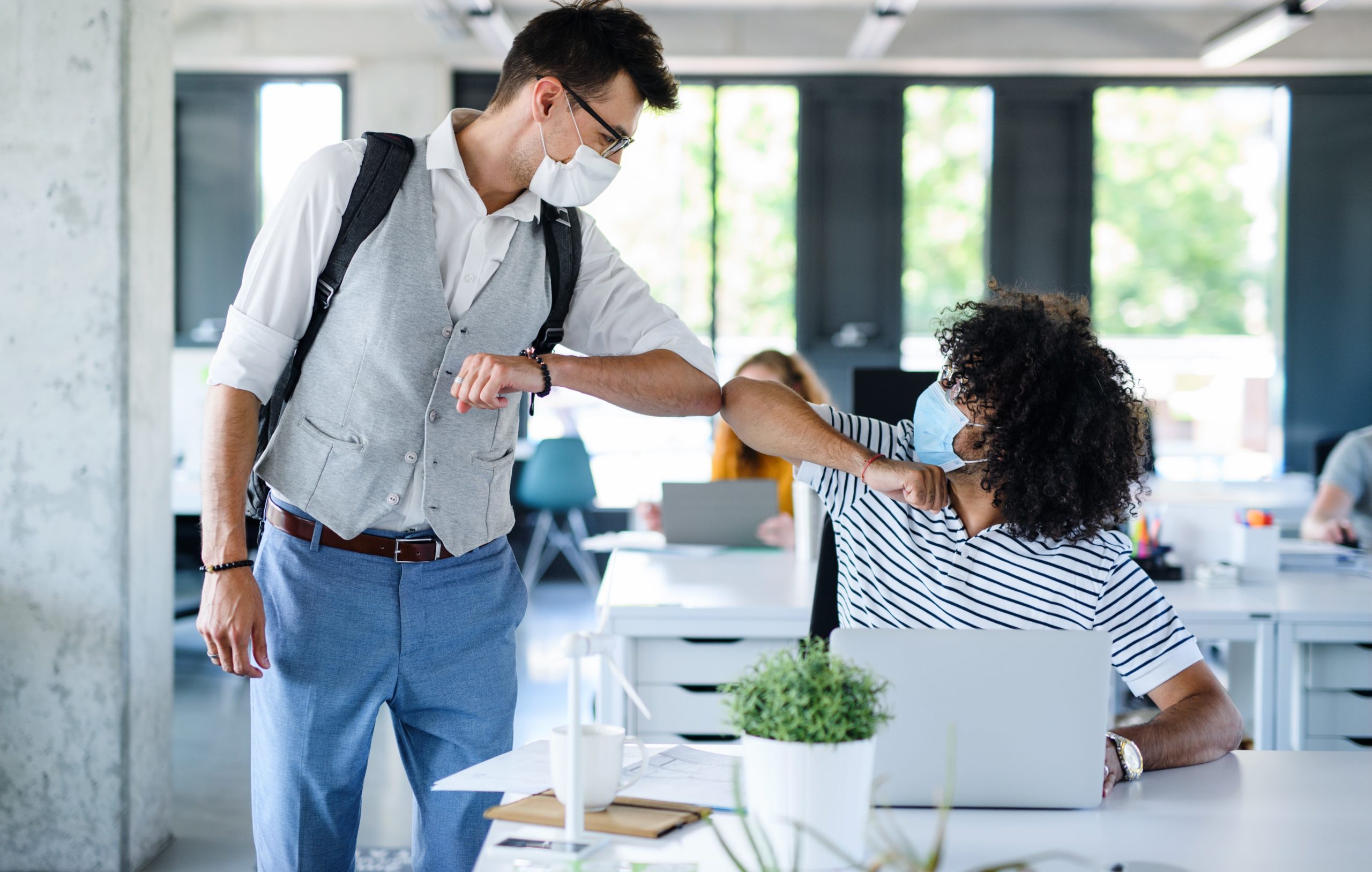 Young people wearing facemasks in office elbow bumping, Covid shared ownership concept