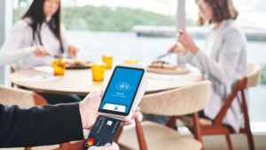 Hand using Square card reader with women having lunch in background, contactless concept