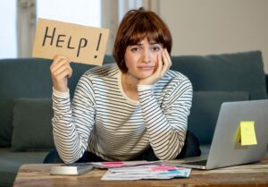 Young woman holding up 'Help' sign by laptop, self-employed tax concept
