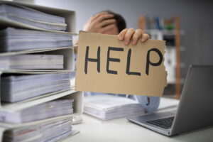 Office worker hemmed in by files holding up help sign, emergency Covid-19 help concept