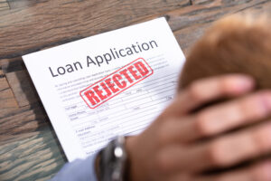 Disbelieving man with head in hands and rejected loan application form, Recovery Loan Scheme concept