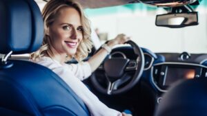 Smiling woman sitting behind car steering wheel looking over shoulder, mileage allowance concept