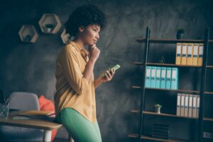 Young black woman pondering smartphone, trading type concept