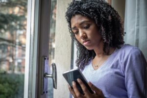 Young black woman worriedly looking at mobile phone, racist tweet concept