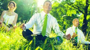 Office workers sitting cross-legged in field meditating, green concept