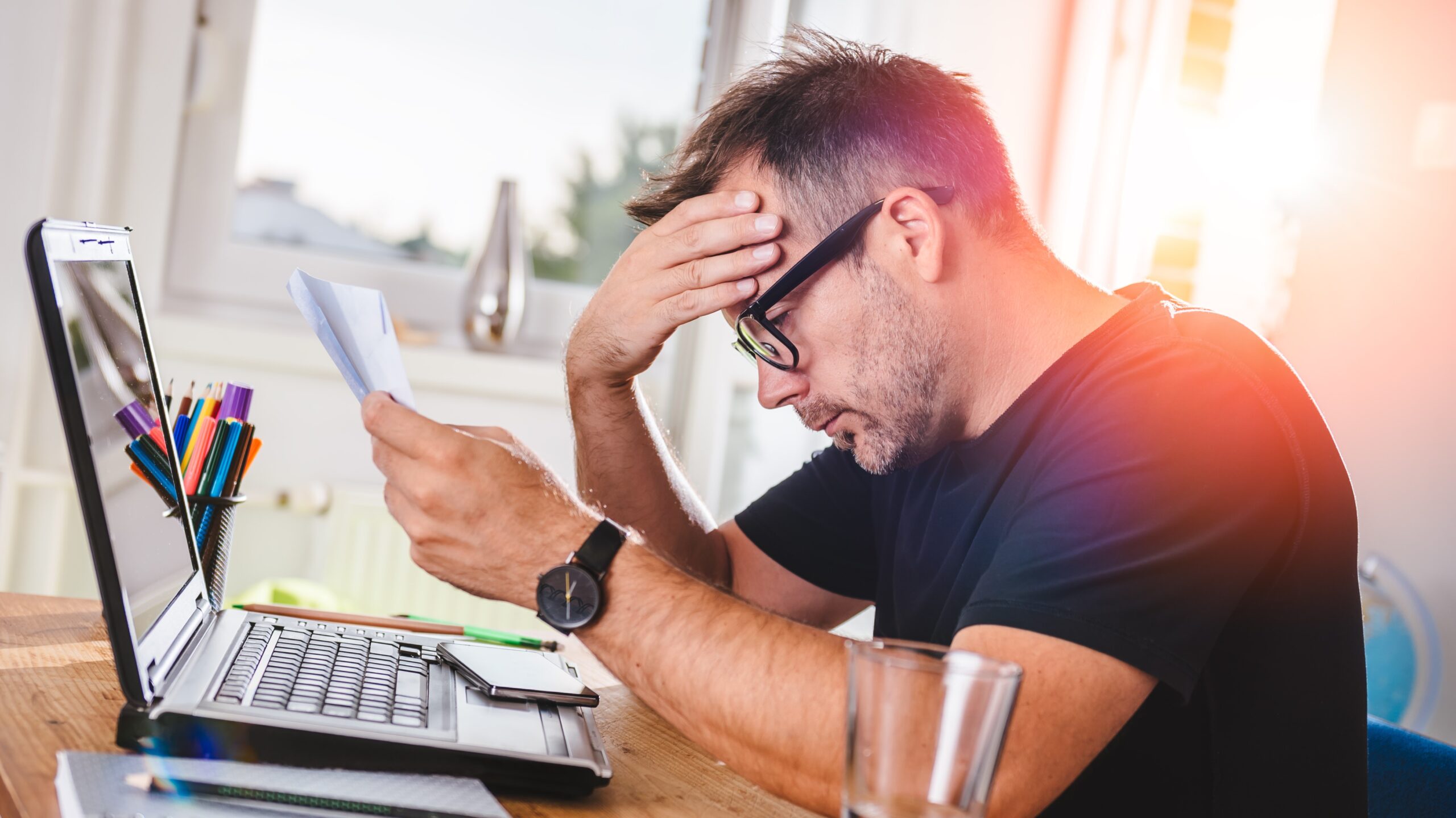 Man holding head in hands as he reads letter over laptop, businesses debt concept
