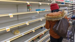 Woman with back to camera surveying empty supermarket shelves, supply chain crisis concept