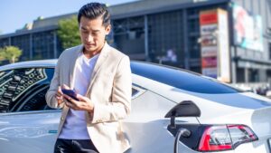 Asian businessman on mobile phone while electric car charges