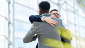 Older businessman hugging younger black colleague, re-employing staff concept