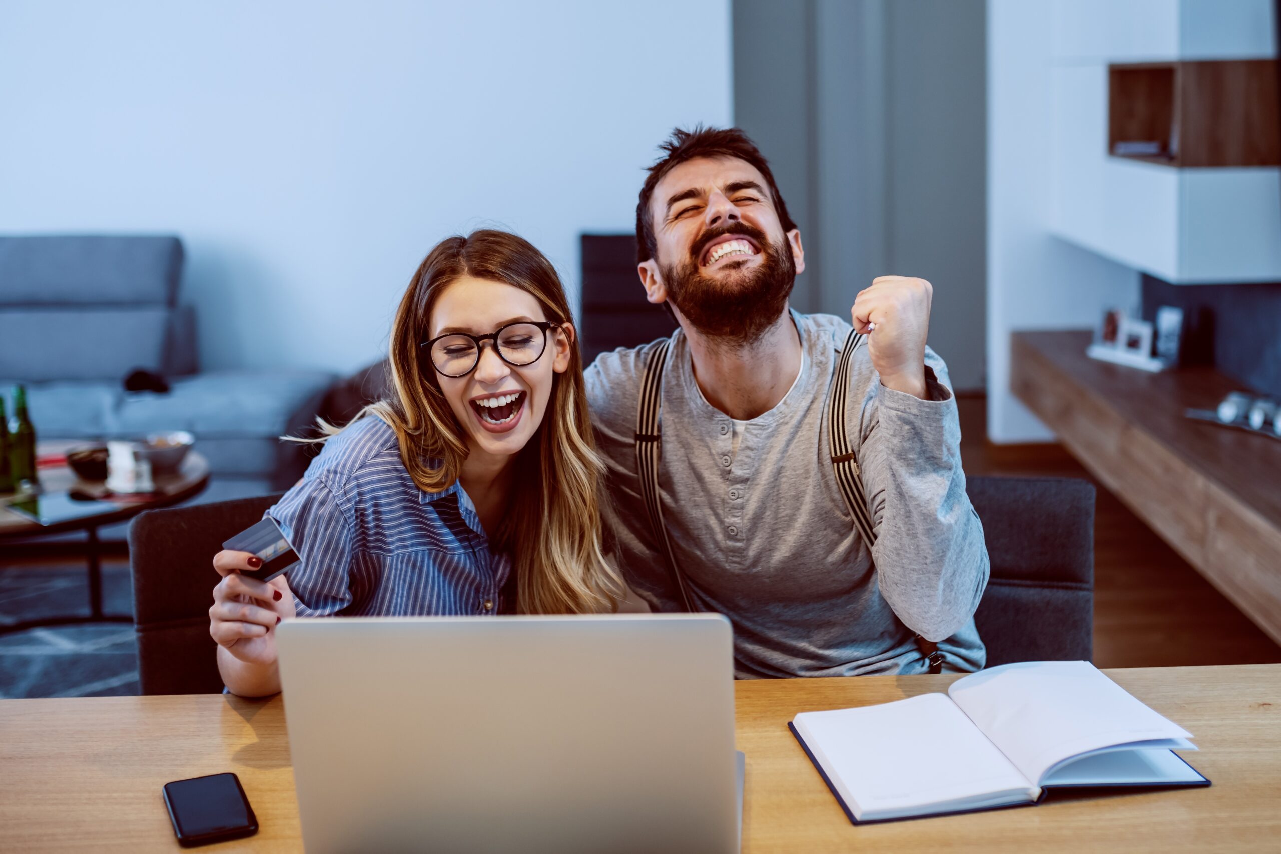 Bearded man fist clenching beside smiling woman wearing glasses both at laptop, staff National Insurance concept