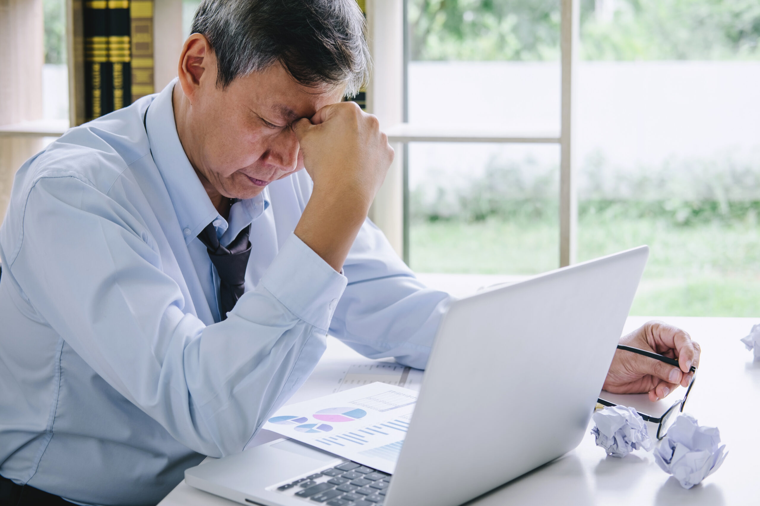 Businessman clutching forehead over laptop, going bust concept