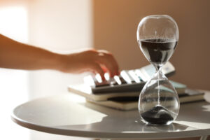 Woman tapping calculator beside hourglass, R&D tax relief concept