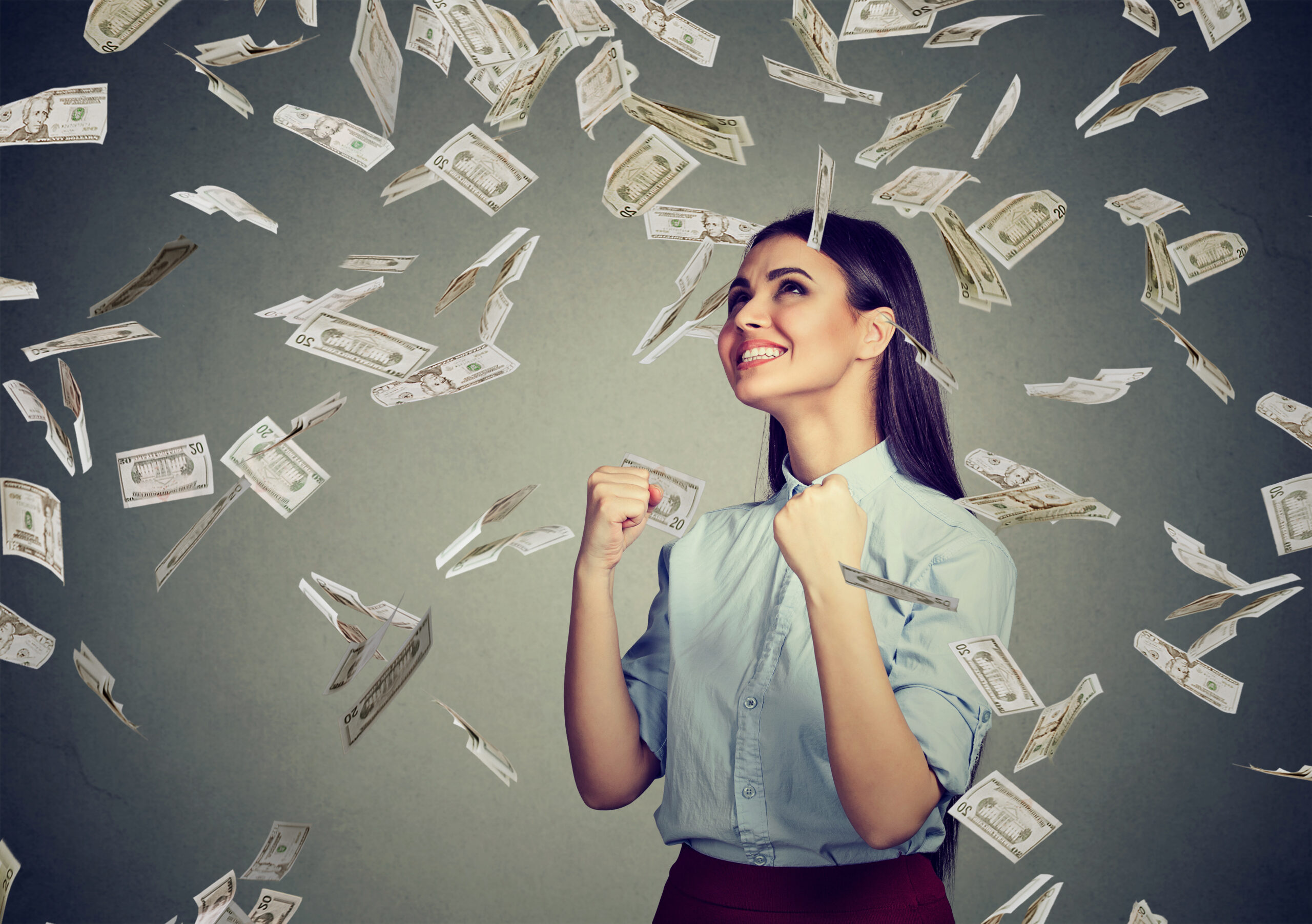 Woman pumping fists being rained on by money, bonus concept