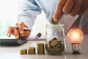 Businessman putting coins in jar while tapping calculator, business energy help concept