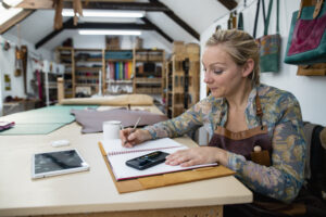 Female leather worker doing calculations by hand at desk, bookkeeping sole trader concept