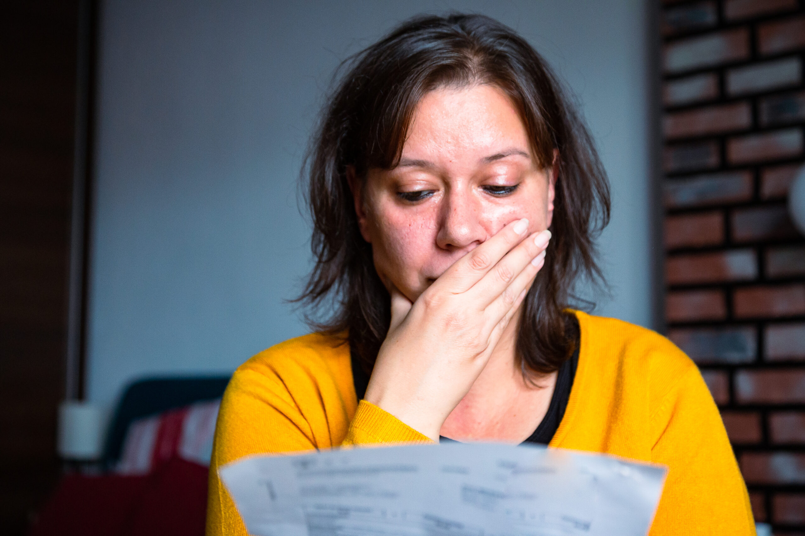 Woman in yellow jumper opening shocking bill, cost of doing business concept