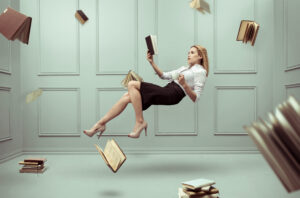 Market your book concept. Pretty woman holding book floating surrounded by other books