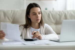 Making Tax Digital self-employed concept. Pensive young woman studies laptop screen doing paperwork