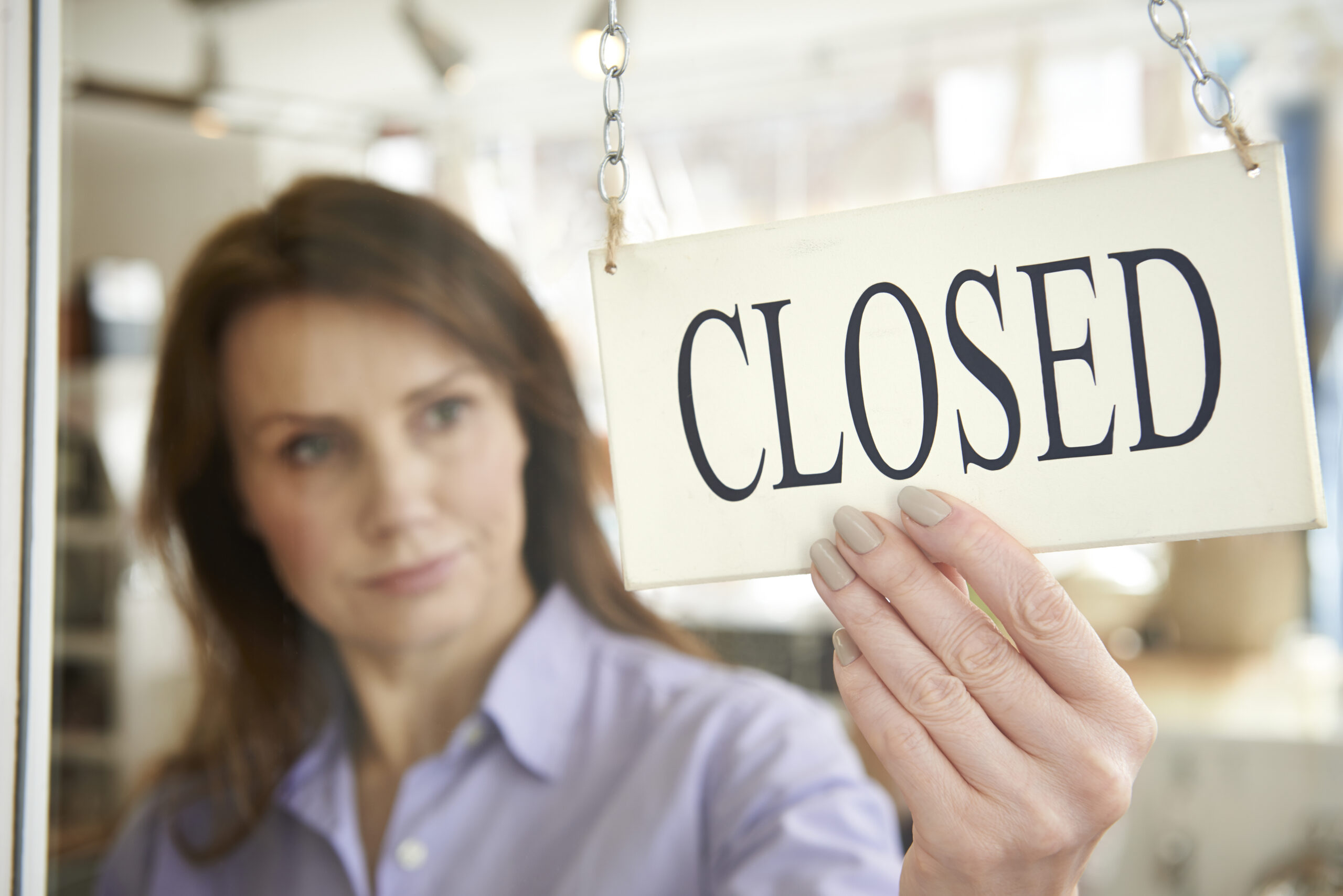 Businesses going under concept. Woman turning Closed sign on shop towards viewer.