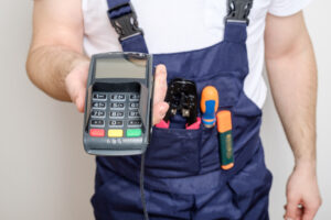 Sole traders VAT concept. Builder wearing tool belt holds out card payment machine