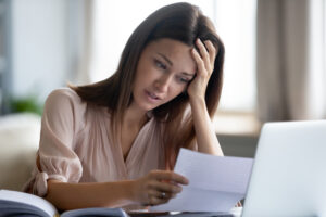 Insolvent redundancy concept. Young woman clutching head reading letter in front of laptop