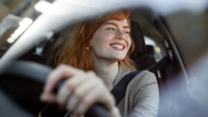 Company car insurance concept. Young redheaded woman behind steering wheel smiling