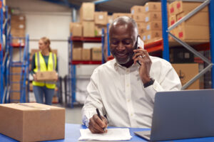 Exports concept. Smiling black businessman on phone taking order in warehouse.