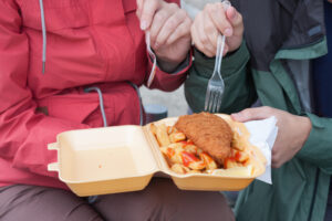 Young couple is eating traditional London food fish and chips from plastic box on street.